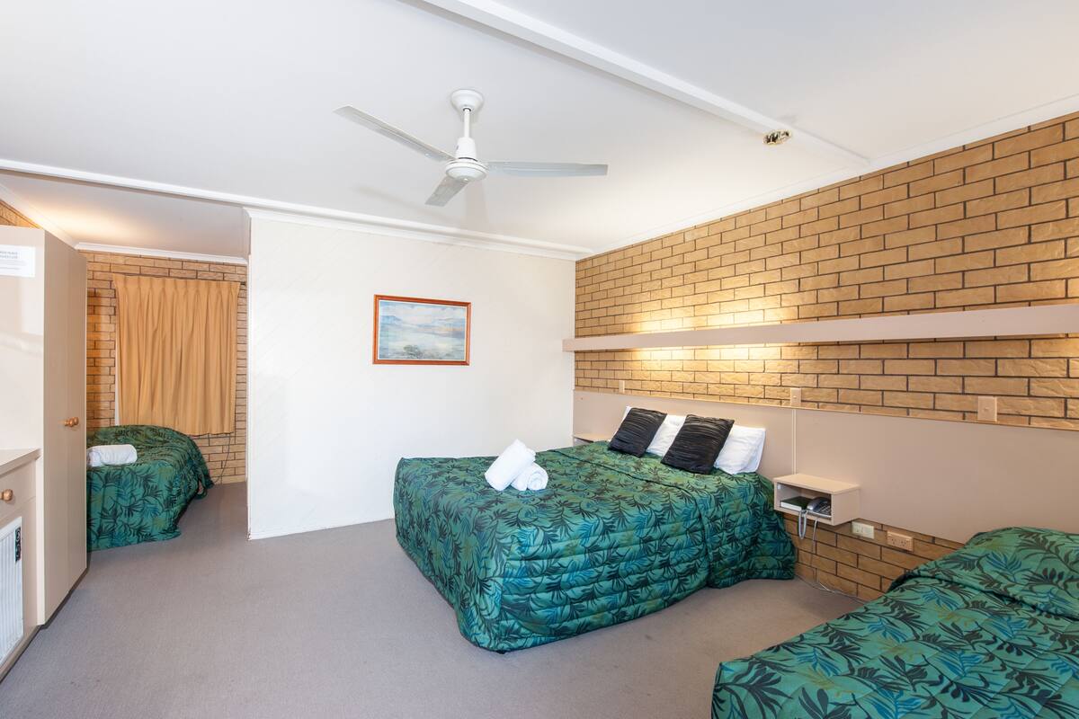 A room with two beds, a ceiling fan, a brick accent wall, and a framed picture on the wall.