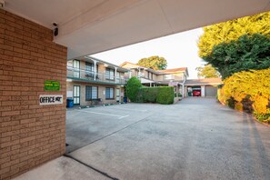 A hotel entrance with a guest laundry service, a parking lot, and a building with multiple floors and balconies. - Jacaranda Place Motor Inn (South Toowoomba)
