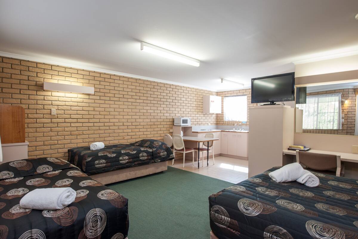 A hotel room with two beds, a desk, a chair, a television, and a brick wall.