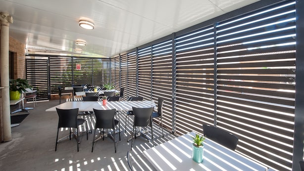 An outdoor patio area with tables and chairs, a brick wall, and a metal fence with horizontal slats.