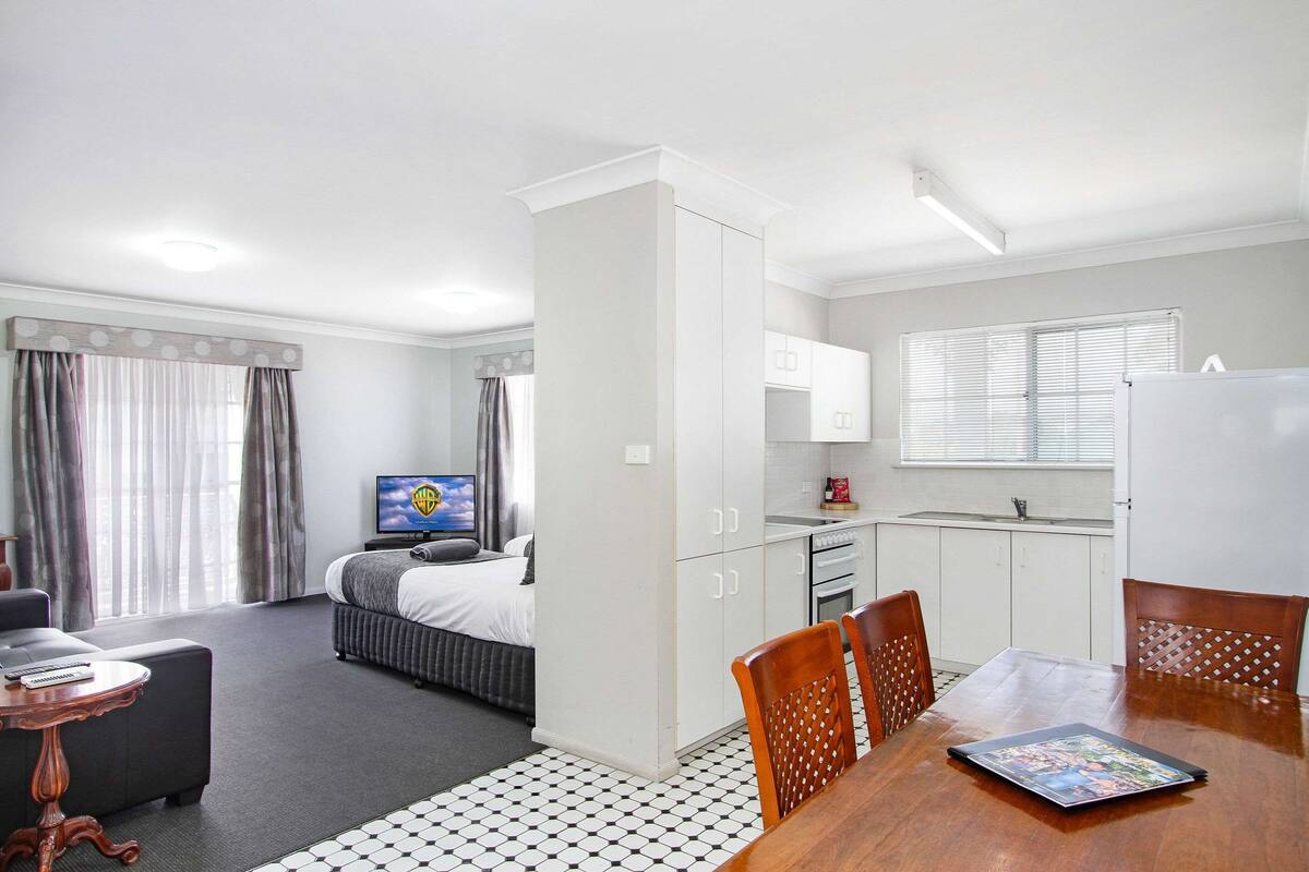 A hotel room with a bed, a desk, a dining table, and a kitchenette.