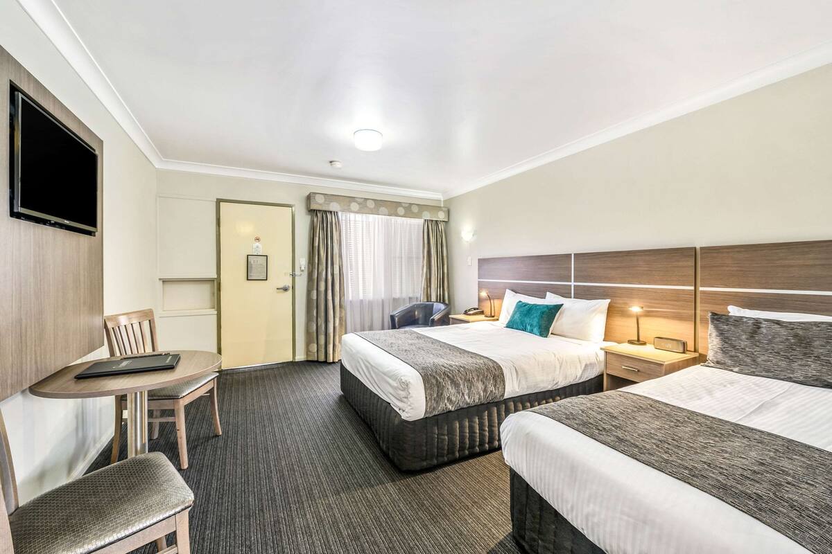 A hotel room with two beds, a desk, a chair, a flat-screen TV, and a door.
