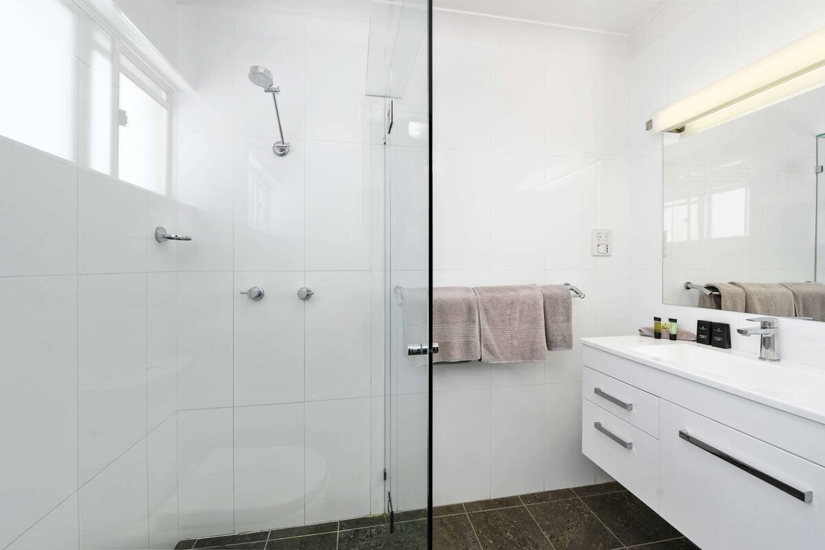 A modern bathroom with a glass shower enclosure, a white vanity with a mirror, and a towel hanging on the wall.