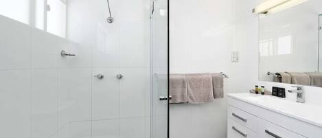 Une salle de bain moderne avec une douche à l’italienne en verre, un meuble-lavabo blanc avec un miroir et une serviette accrochée au mur.