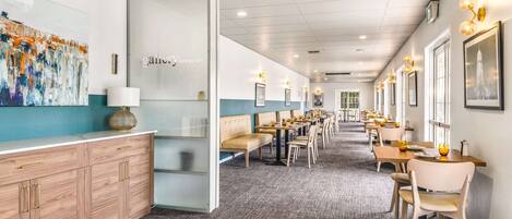 A modern restaurant with a long counter, cushioned seating, and framed artwork on the walls.