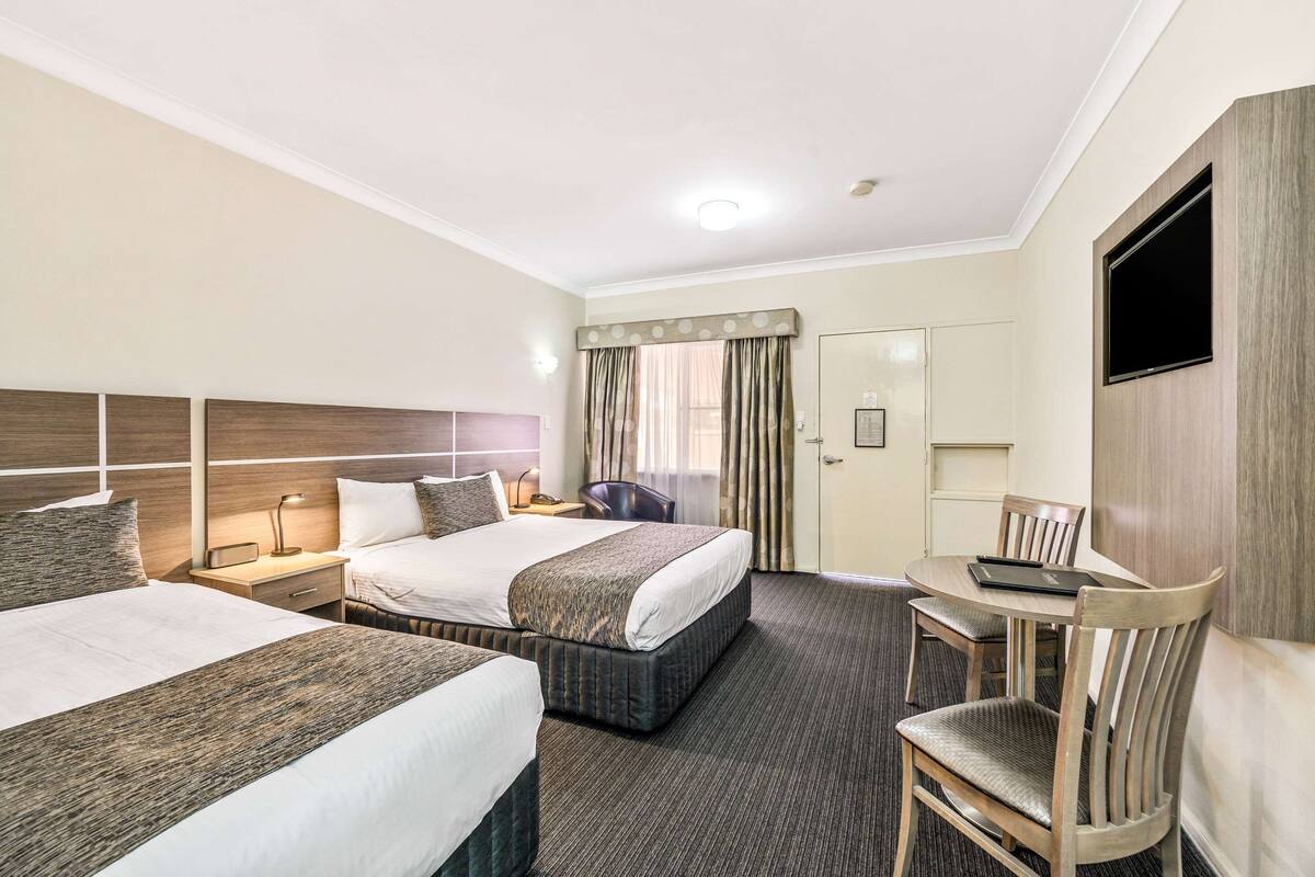 A hotel room with two beds, a desk, a chair, a TV, and a bathroom door.