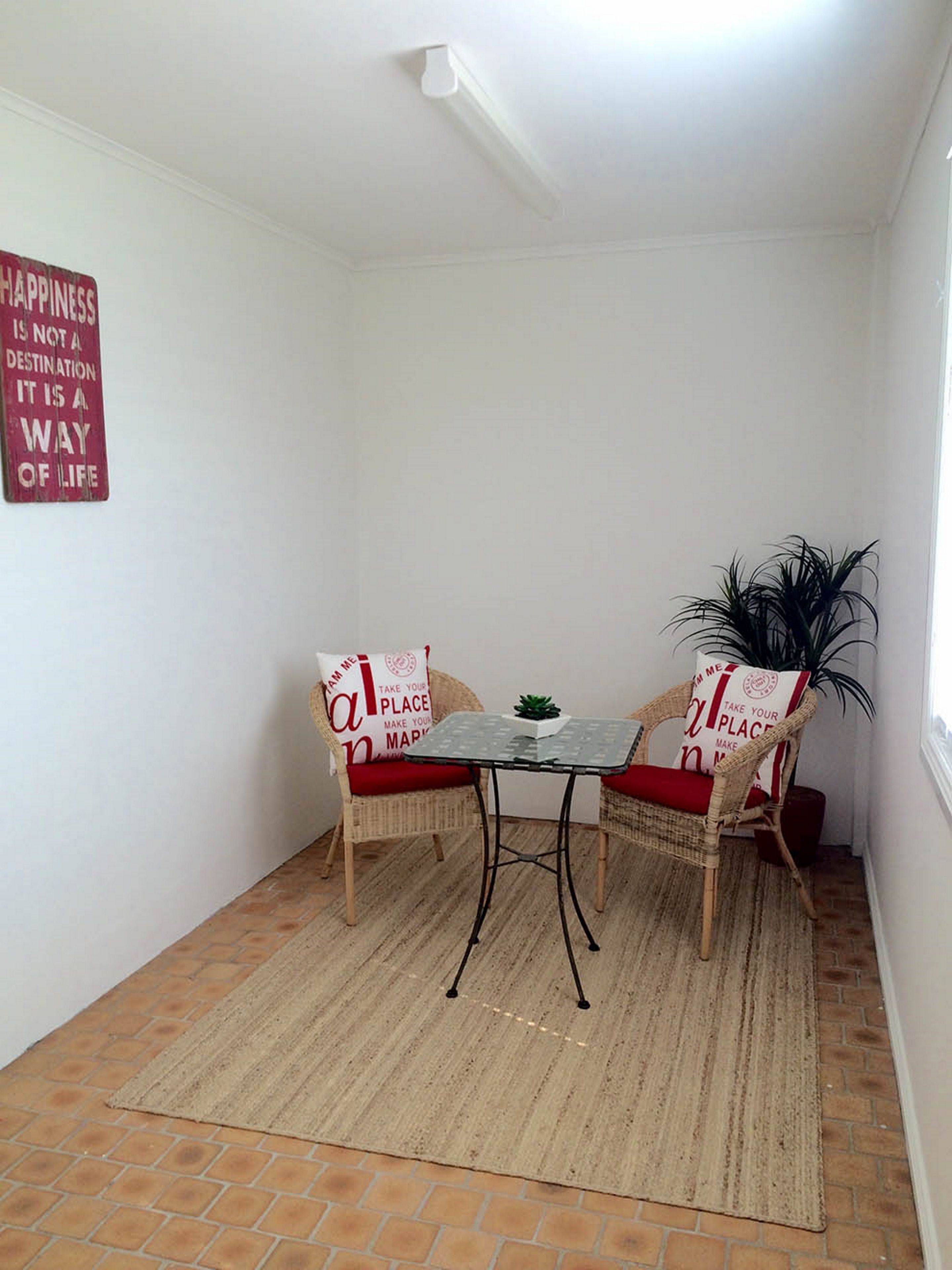 A small room with two wicker chairs, a small table, and a red sign on the wall.
