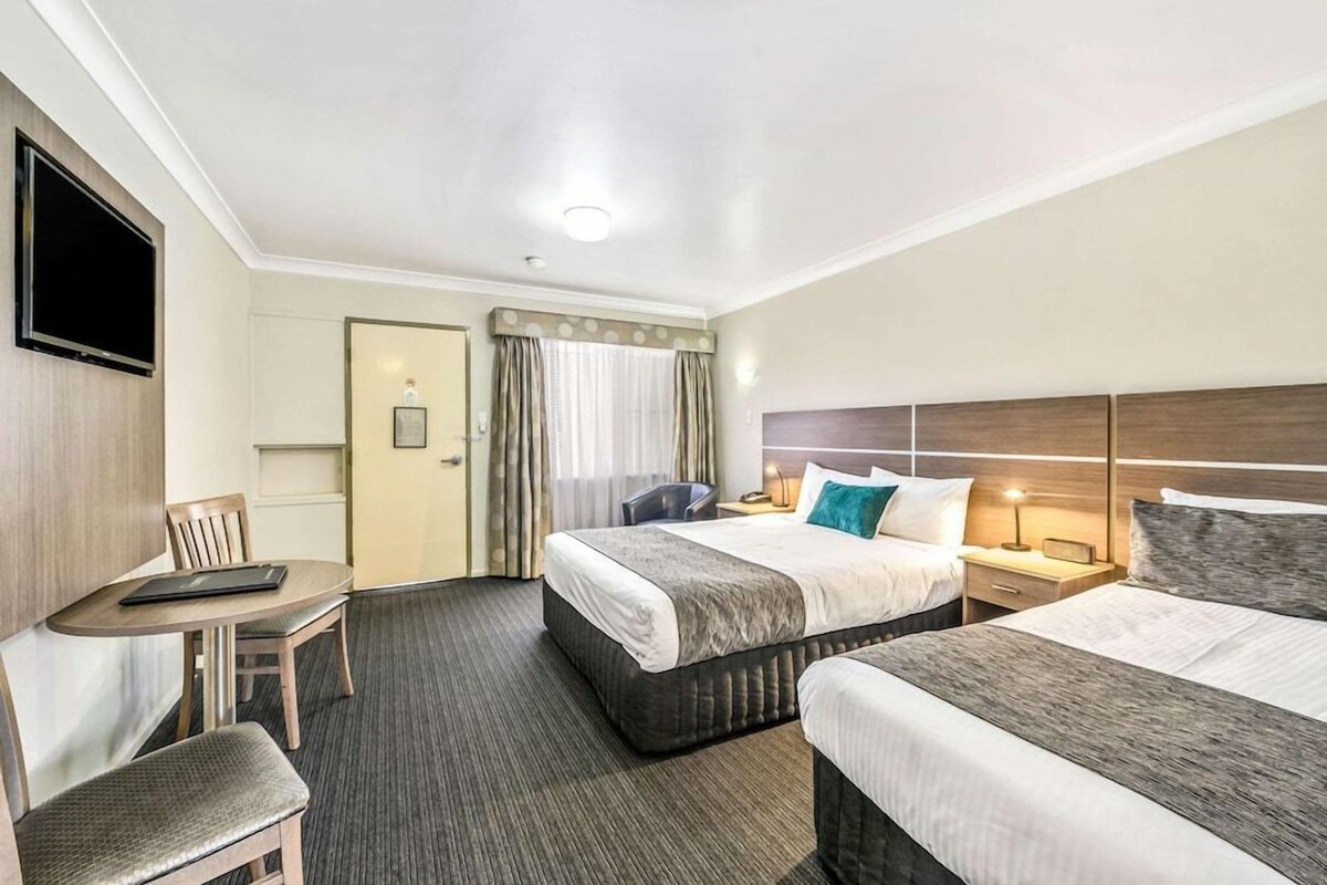 Ein Hotelzimmer mit zwei Betten, einem Schreibtisch, einem Stuhl, einem Fernseher und einer Tür.