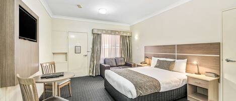Une chambre d’hôtel avec un grand lit, un bureau avec une chaise, un téléviseur fixé au mur et une table de chevet avec une lampe.