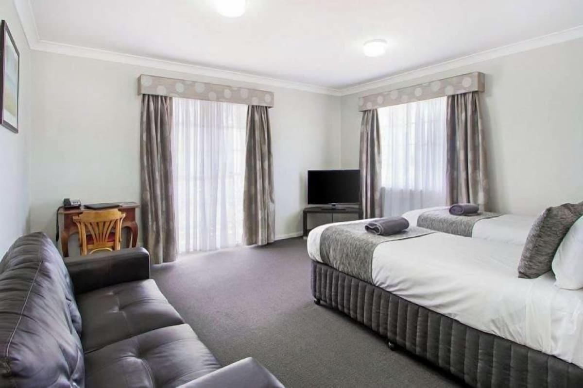 Ein Hotelzimmer mit einer Couch, zwei Betten, einem Fernseher und Vorhängen.