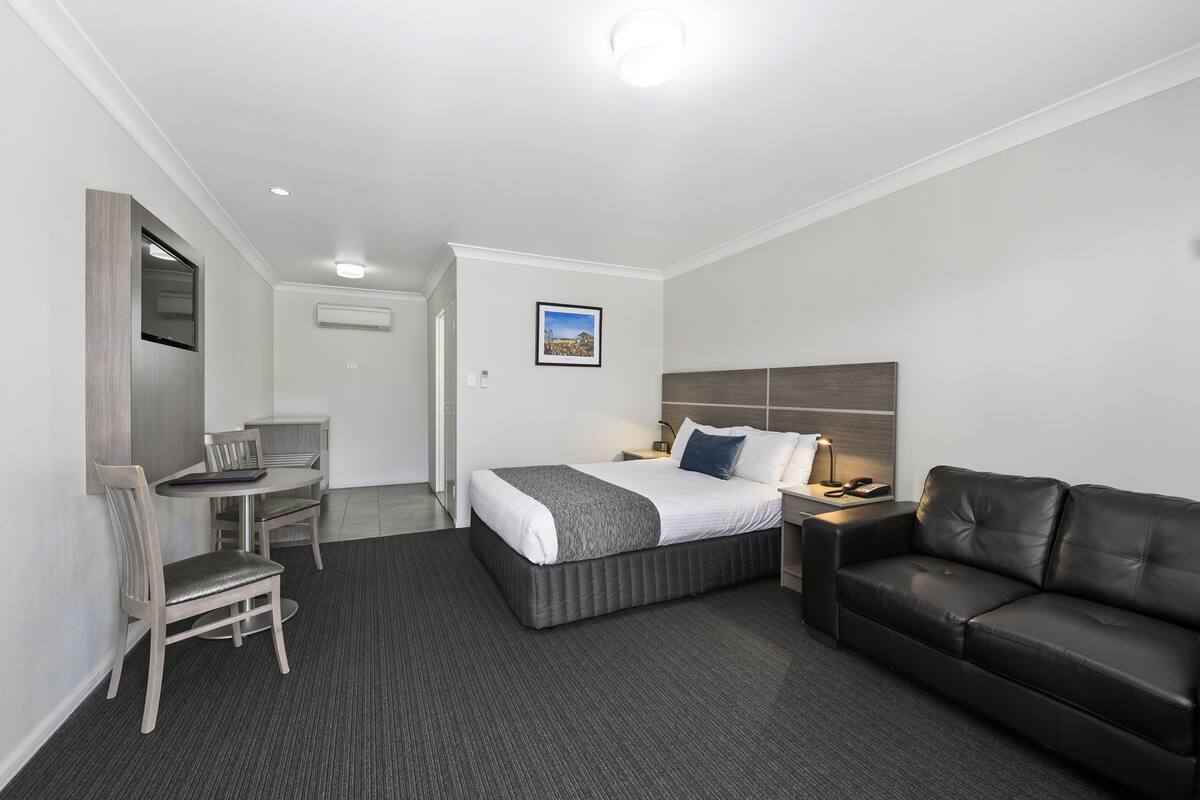 A hotel room with a bed, a desk, a chair, a couch, and a picture on the wall.