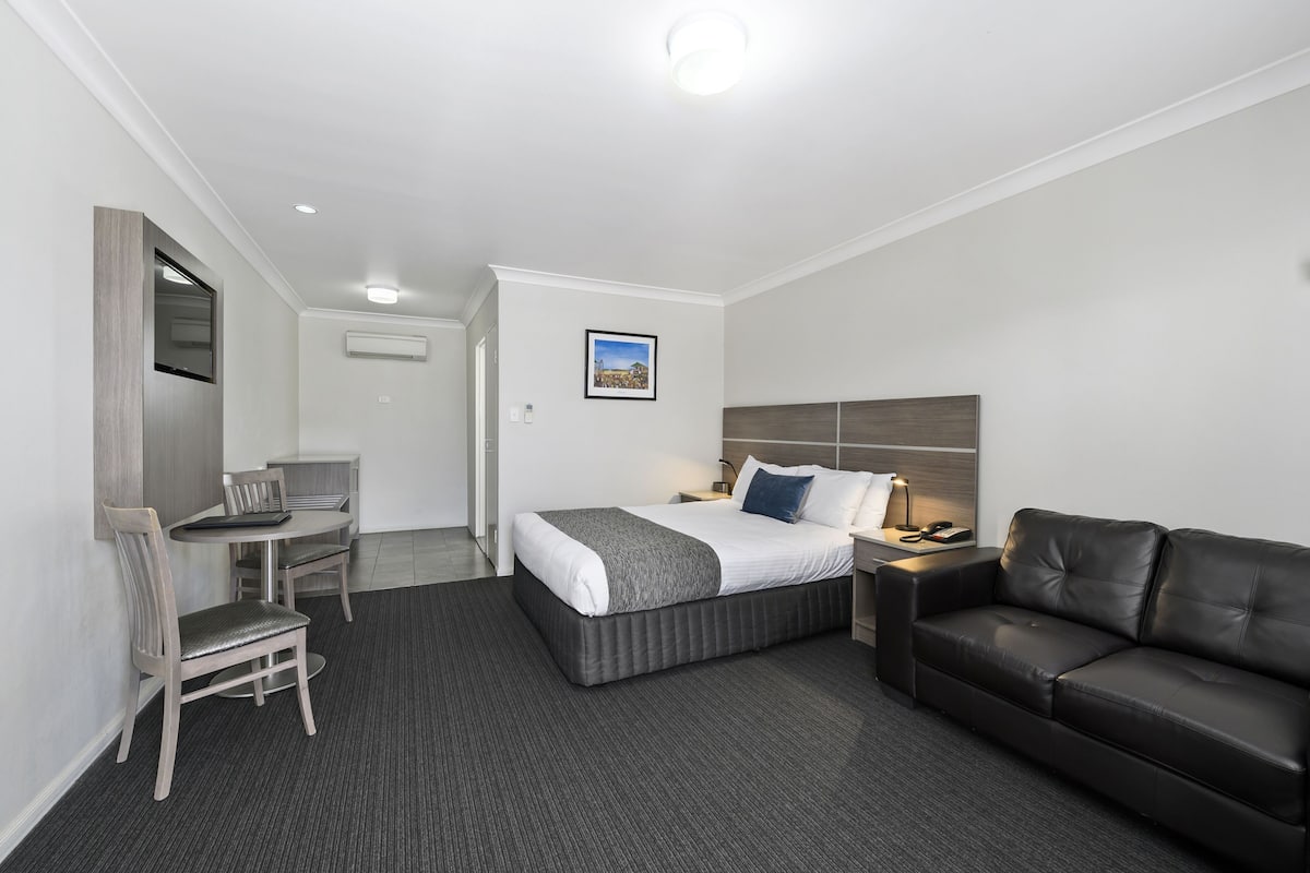 A hotel room with a bed, a desk, a chair, a couch, and a picture on the wall.