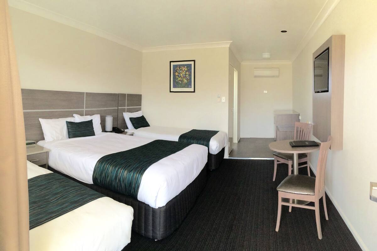 A hotel room with two beds, a desk, a chair, a TV, and a framed picture on the wall.