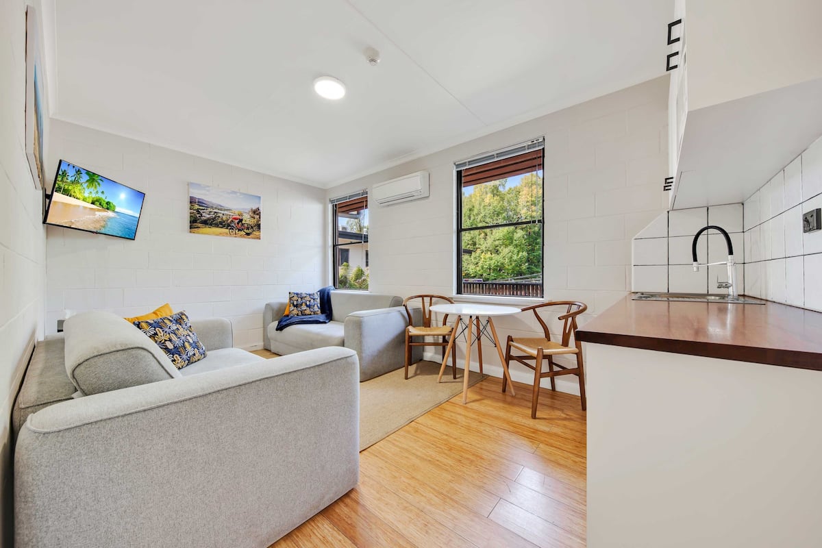A modern living room with a grey sofa, a coffee table, and a dining area with wooden chairs and a white table.
