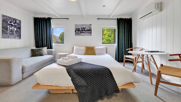 A modern hotel room with a large bed, a sofa, a small round table, and two chairs.