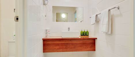 A bathroom with white tiles, a wooden vanity, a mirror, a towel rack, and a toilet.