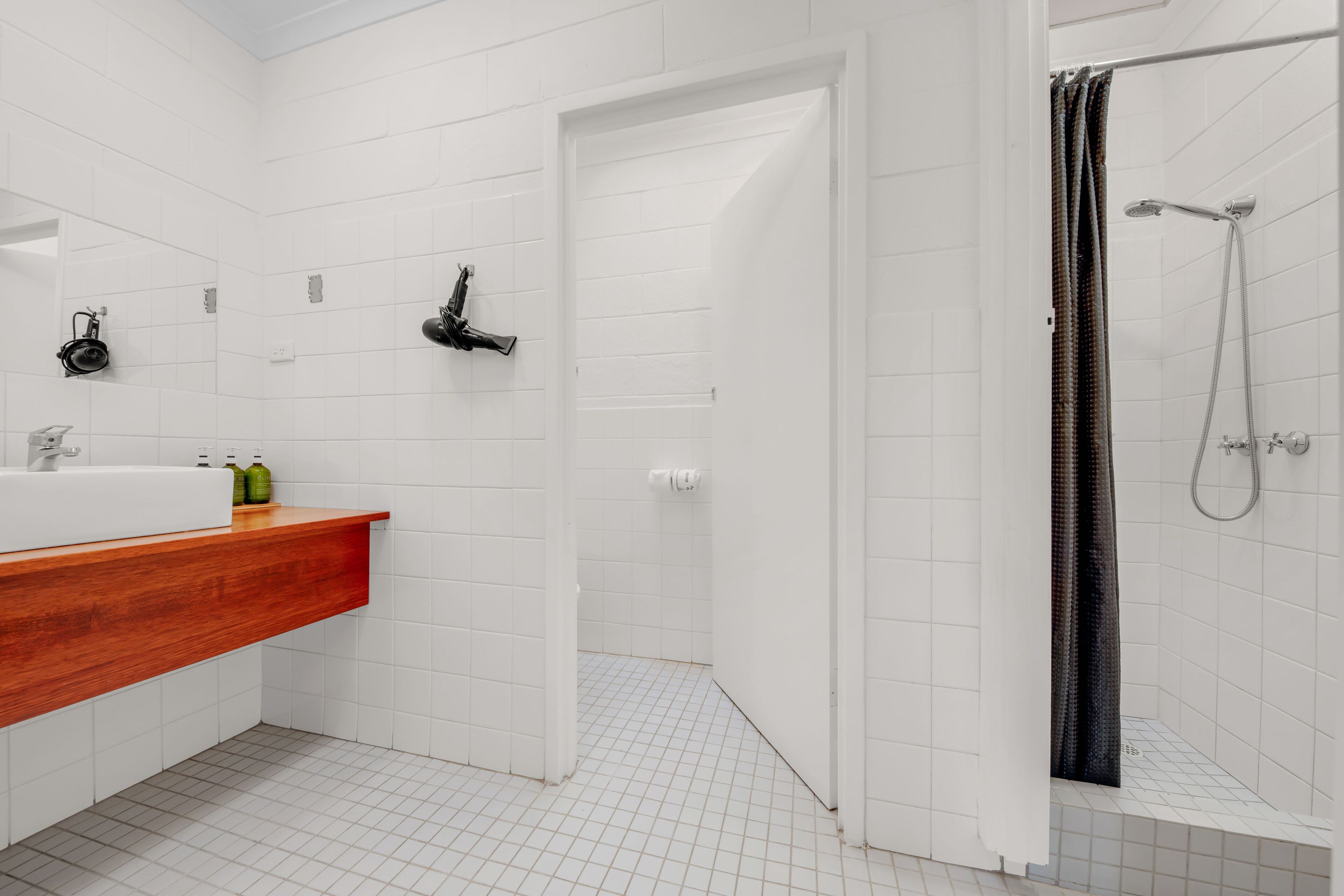Une salle de bain moderne avec des carreaux blancs, un meuble-lavabo en bois, une douche avec un rideau noir et une porte blanche.