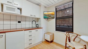 A modern kitchen with white cabinets, a microwave, a sink, and a wooden chair.