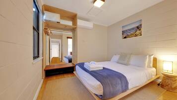 A modern hotel room with a large bed, a wooden headboard, a small bedside table with a lamp, a mirror, and a window with a view of the mountains.