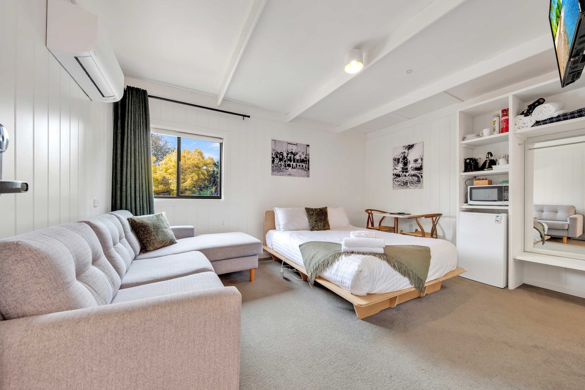 A modern hotel room with a sofa, a bed, a desk, and a TV.