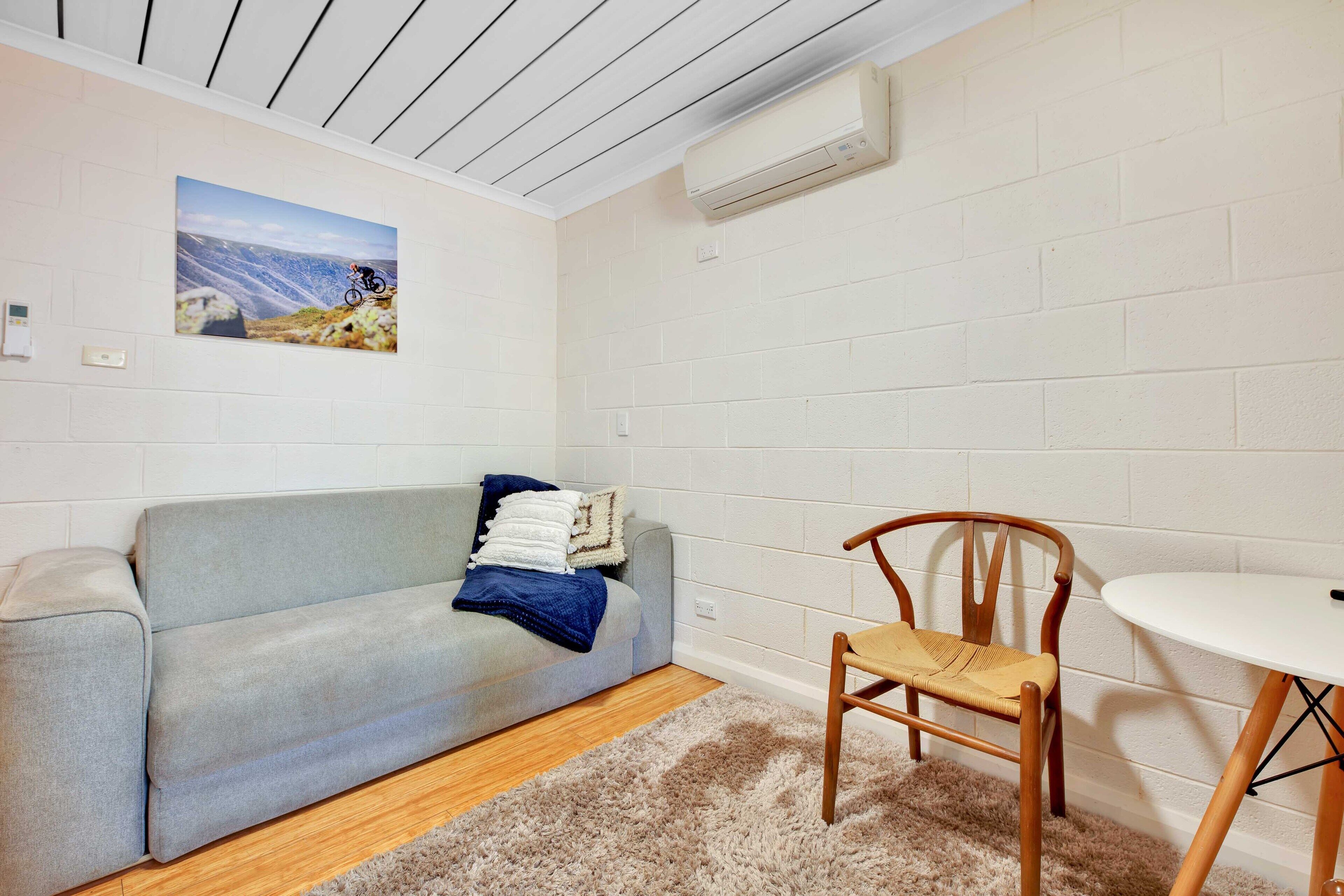 Una habitación con un sofá gris, una silla de madera, una mesa blanca y una alfombra mullida.