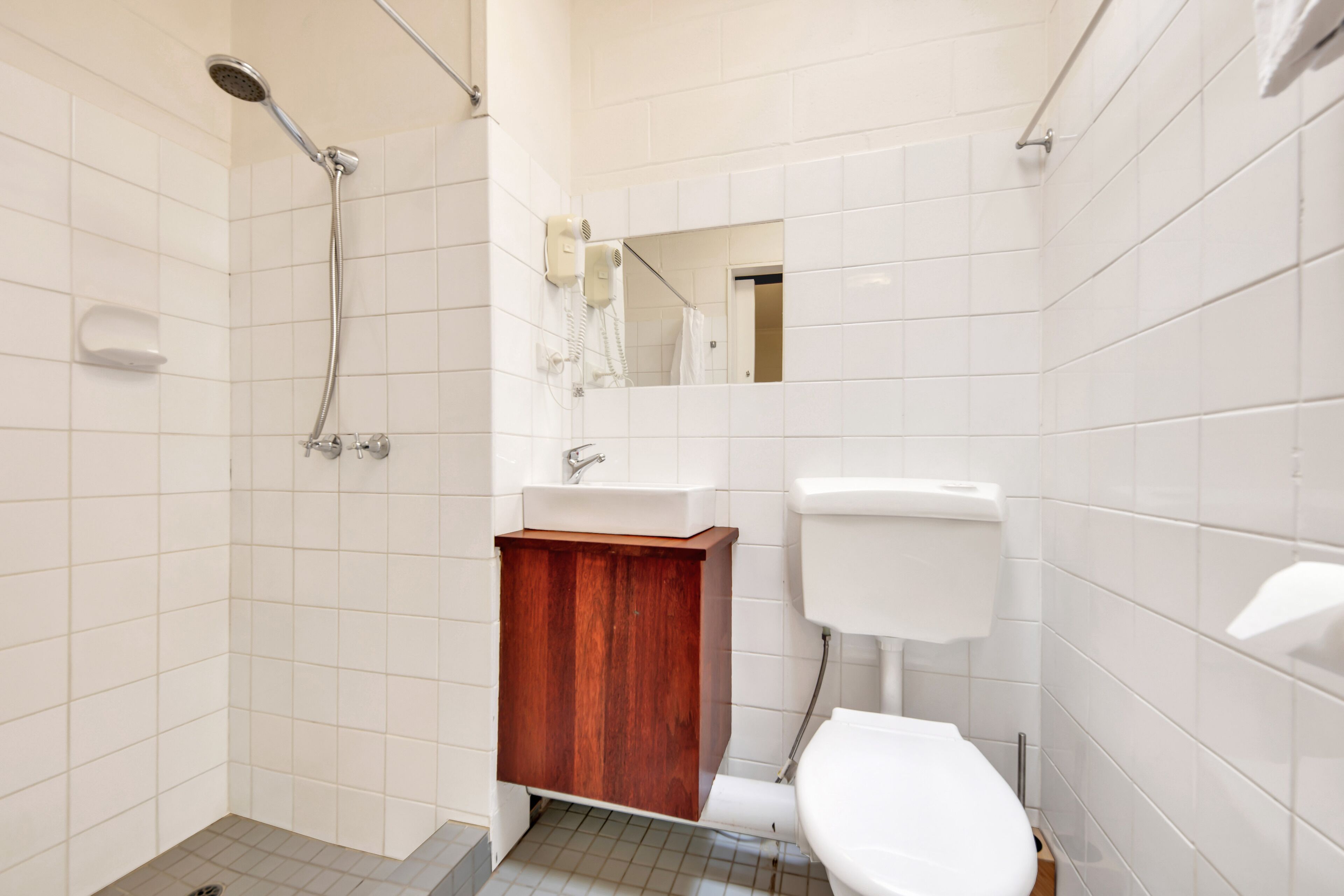 Un baño con ducha, lavamanos, inodoro y un armario de madera.