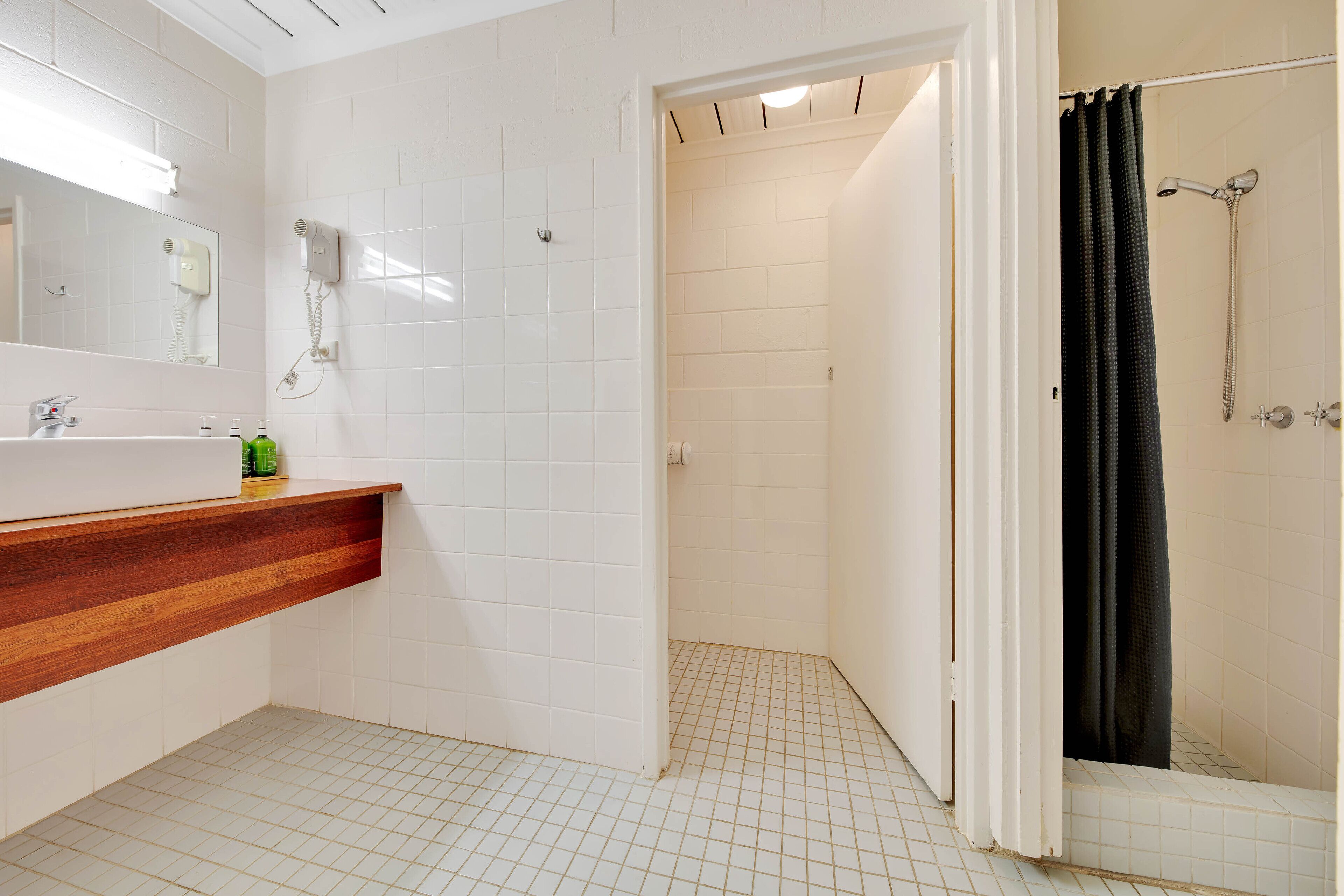 Un baño con tocador de madera, secador de pelo y ducha con cortina negra.