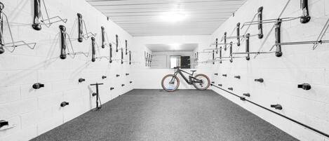 Una habitación larga y estrecha con paredes de ladrillo blanco y alfombra gris. Hay varios soportes para bicicletas a lo largo de las paredes, y una bicicleta estacionada en el centro.