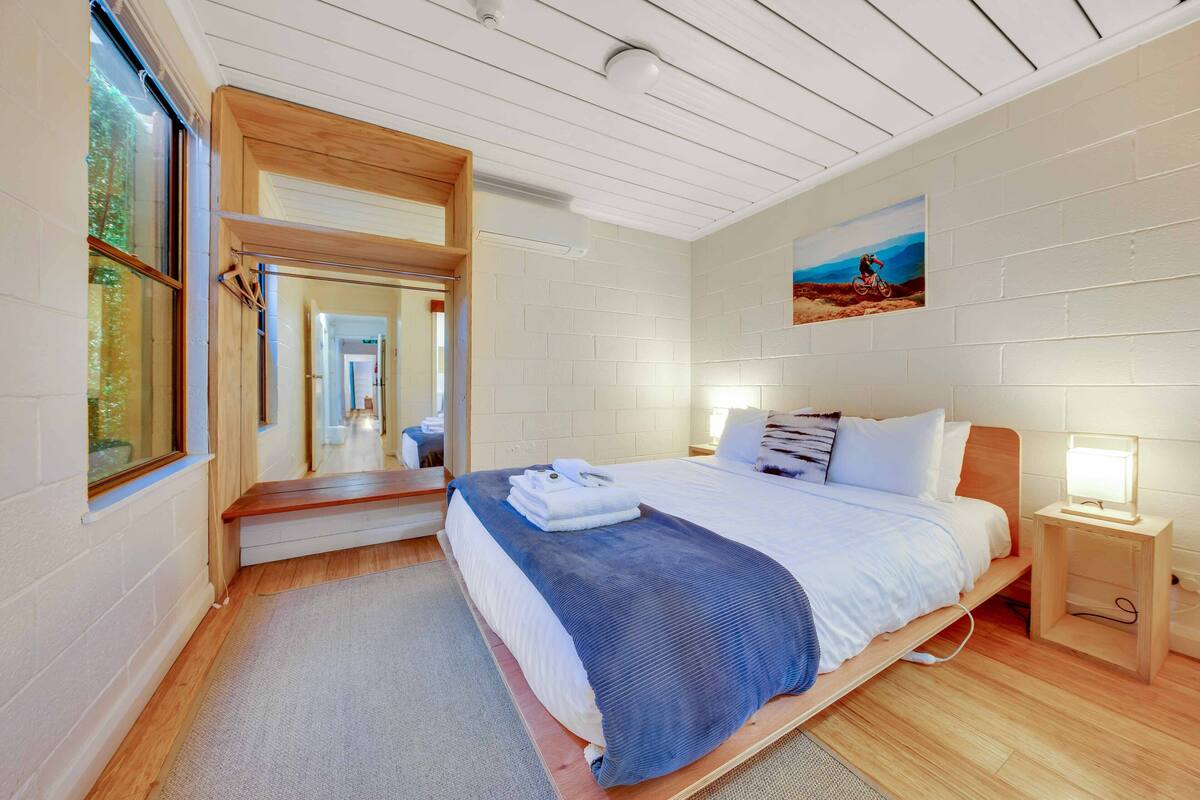 A modern bedroom with a large bed, wooden headboard, a bedside table with a lamp, and a painting on the wall.