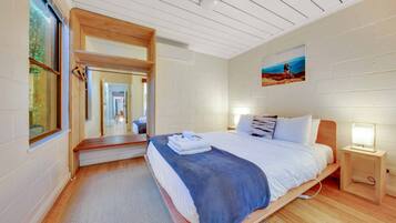 A modern bedroom with a large bed, wooden headboard, a bedside table with a lamp, and a painting on the wall.