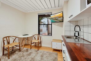 A compact kitchen with a wooden dining table and chairs, a small white cabinet, and a window with a view of a cityscape.