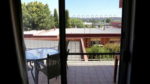 A balcony with a metal table and chairs, a view of a parking lot, and a building with a red roof. - Westwood Motor Inn (Armidale)