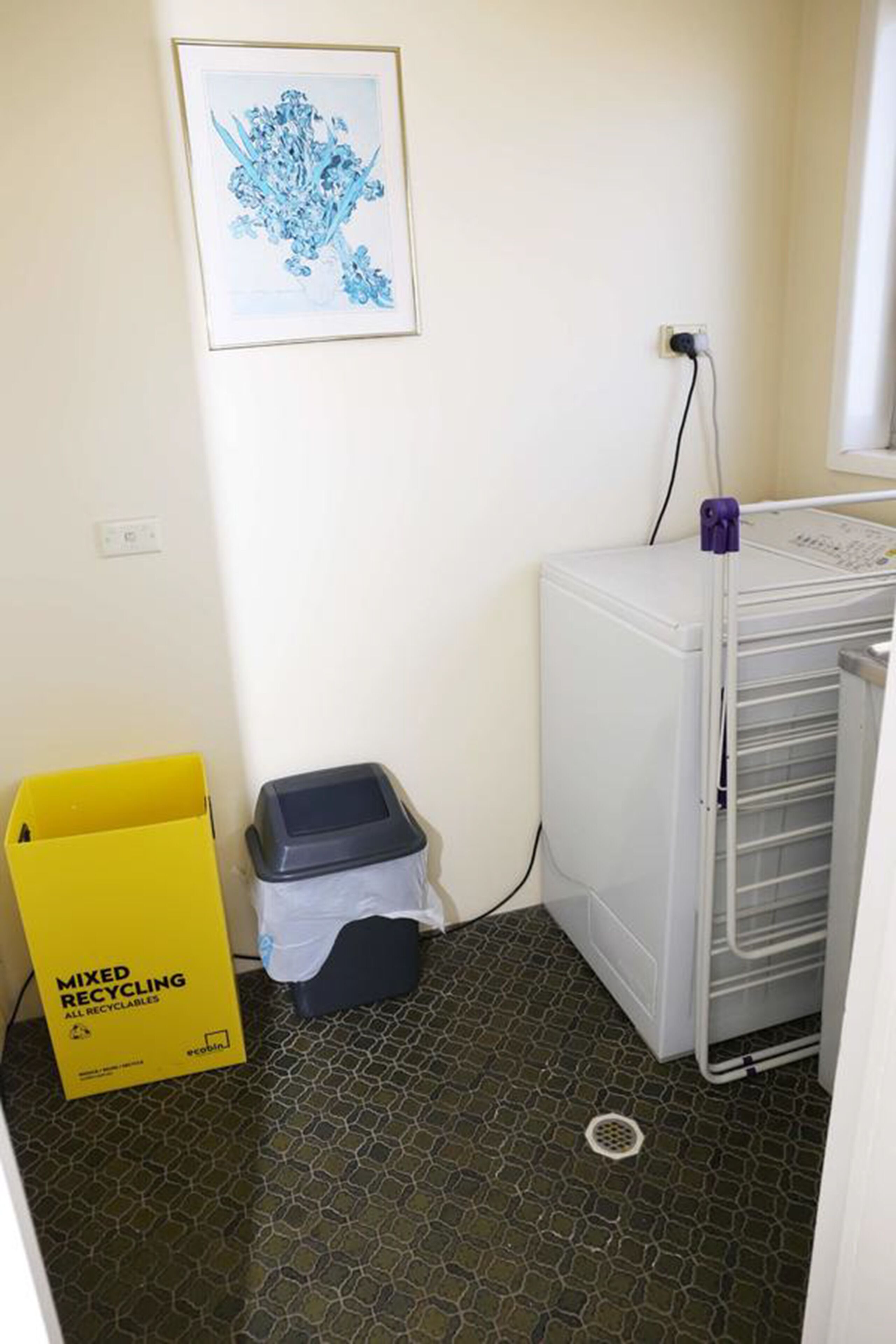 Ein Waschraum mit Waschmaschine, Wäscheständer, Mülleimer und Recyclingbehälter.