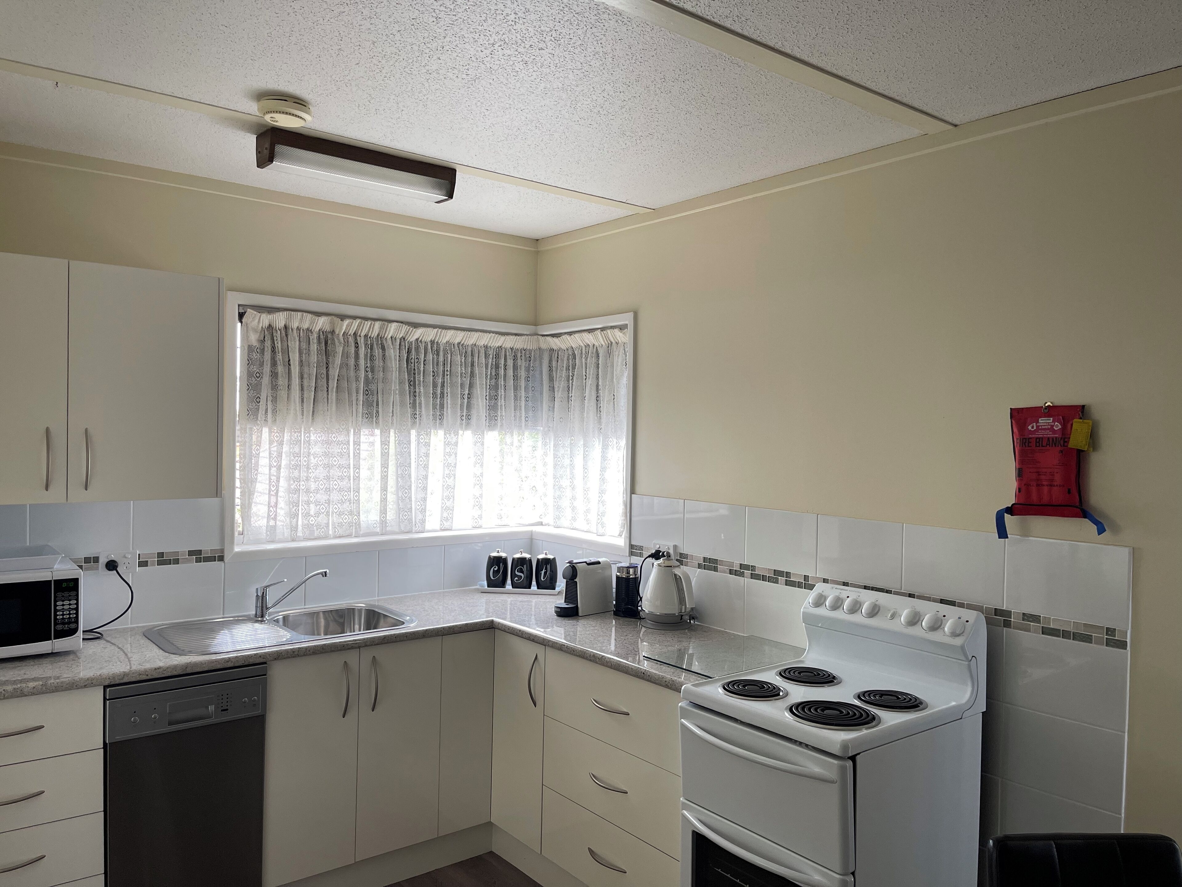 A kitchen with white cabinets, a stove, a microwave, and a window with patterned curtains.