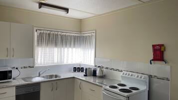 A kitchen with white cabinets, a stove, a microwave, and a window with patterned curtains.
