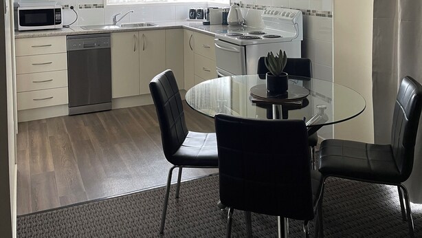 A compact kitchen with a microwave, toaster, kettle, and sink. There is a dining area with a glass table and chairs. - Westwood Motor Inn (Armidale)