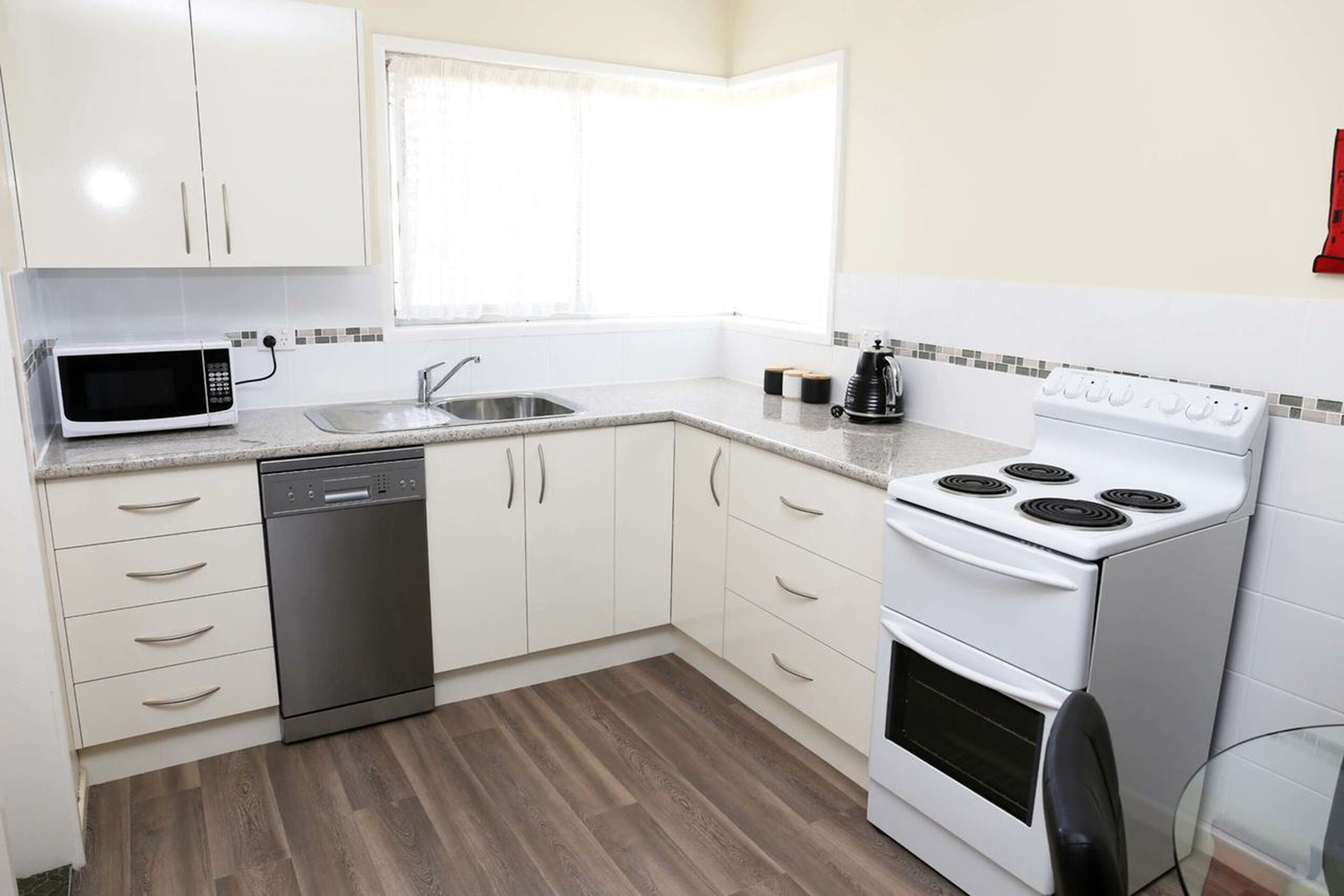 Una cocina moderna con armarios blancos, un lavavajillas de acero inoxidable, un microondas, una estufa y un fregadero.