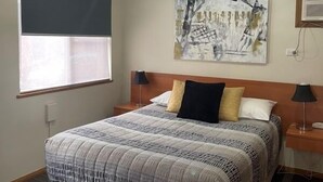 A hotel room with a large bed, two bedside tables with lamps, a window with blinds, and a wall art piece. - Westwood Motor Inn (Armidale)