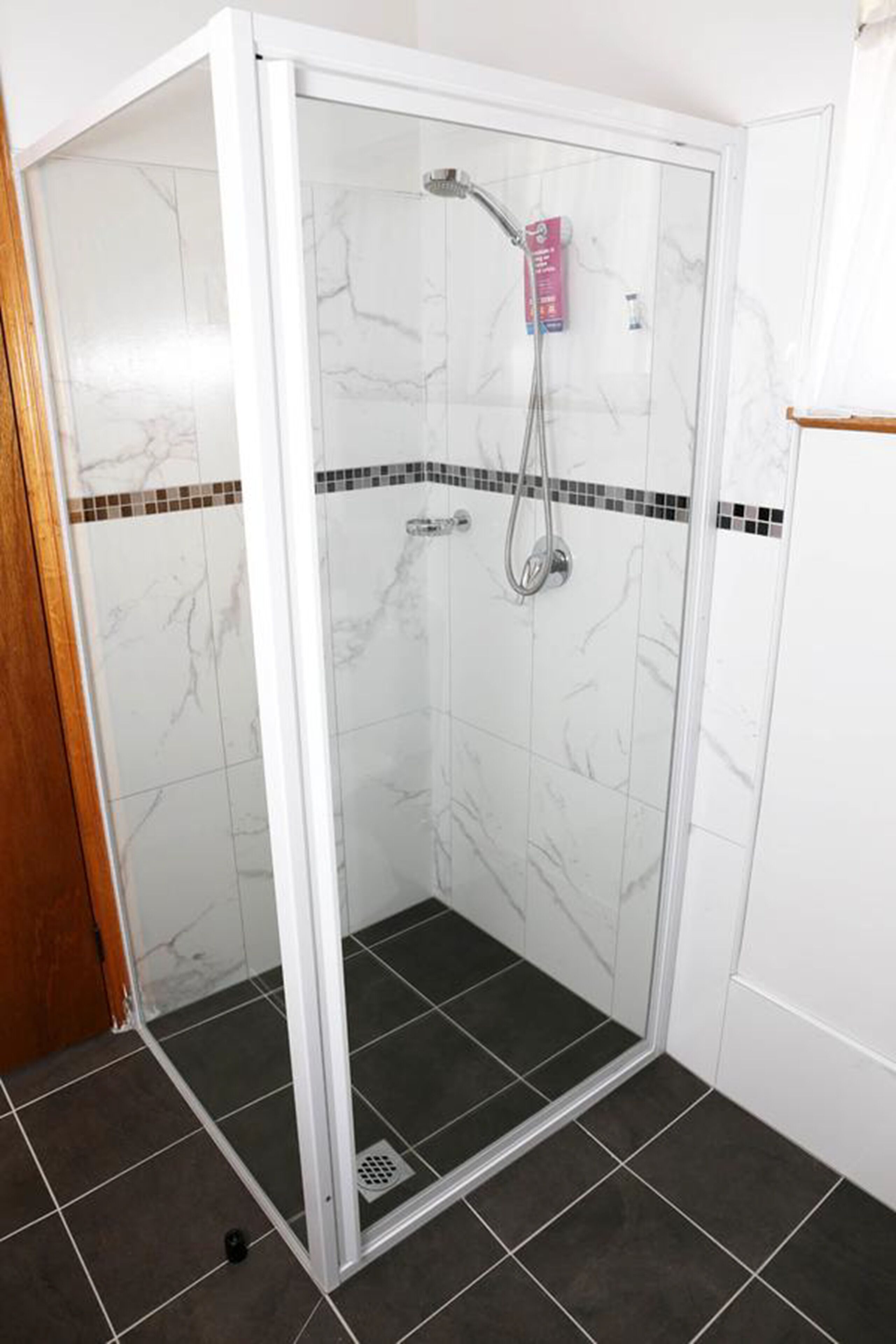 A glass-enclosed shower with a handheld showerhead and a handheld faucet.