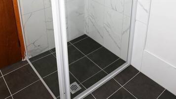 A glass-enclosed shower with a handheld showerhead and a handheld faucet.