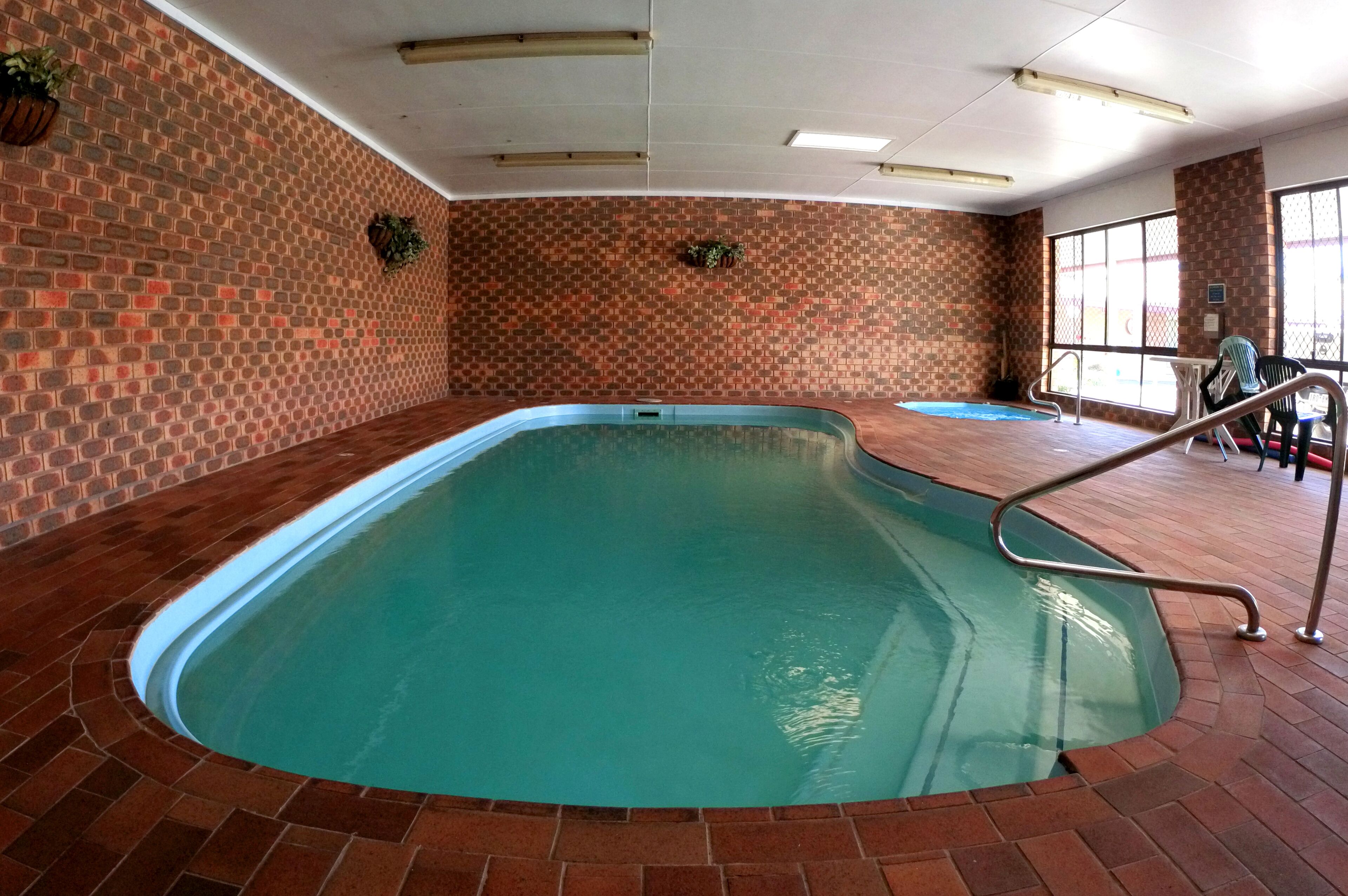 Una piscina interior con pared de ladrillo y barandilla de metal.