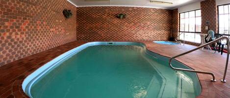 Una piscina interior con pared de ladrillo y barandilla de metal.