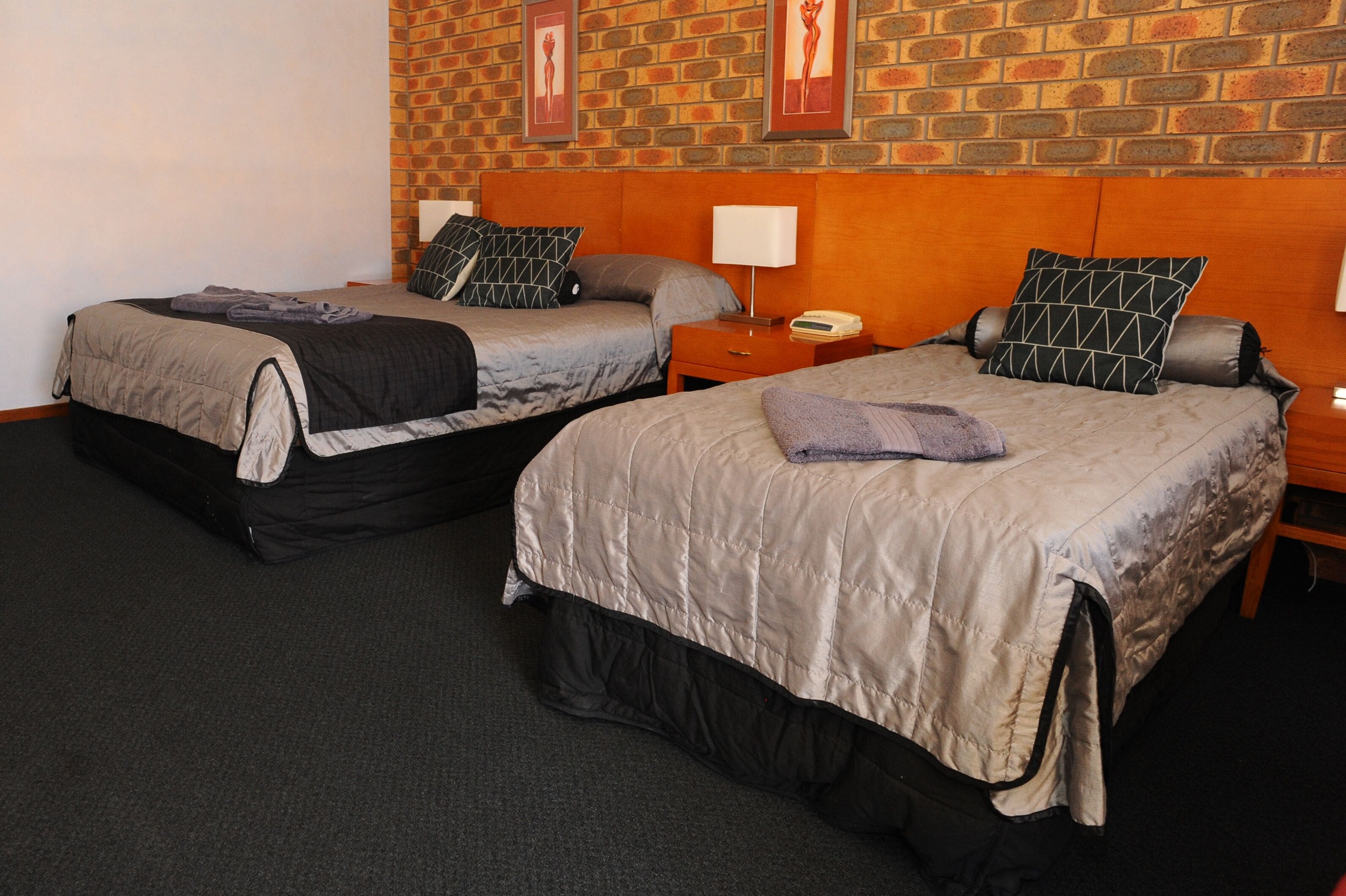A hotel room with two beds, a brick wall, and framed artwork.