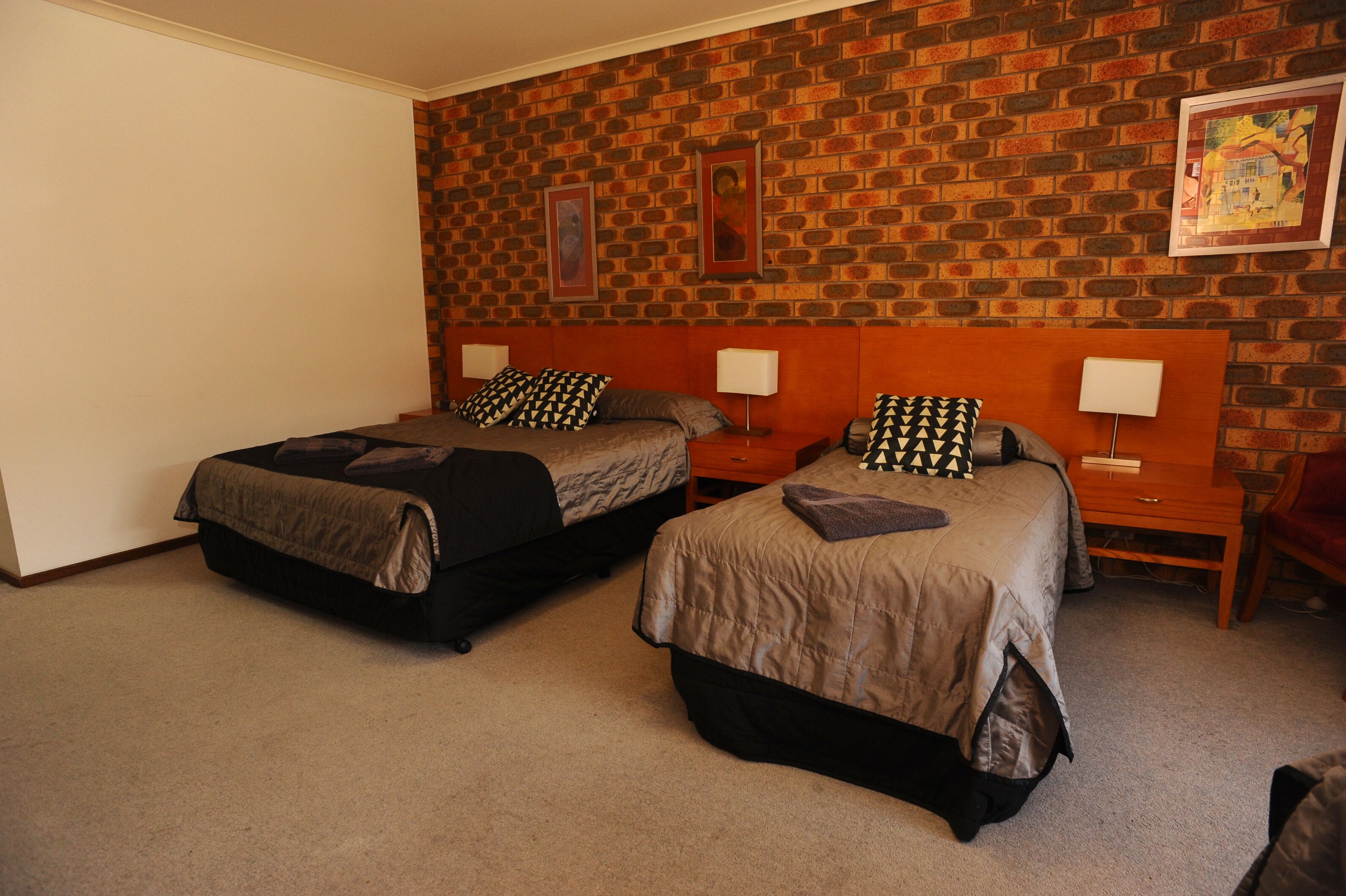 A hotel room with two beds, a brick-patterned wall, and framed artwork.