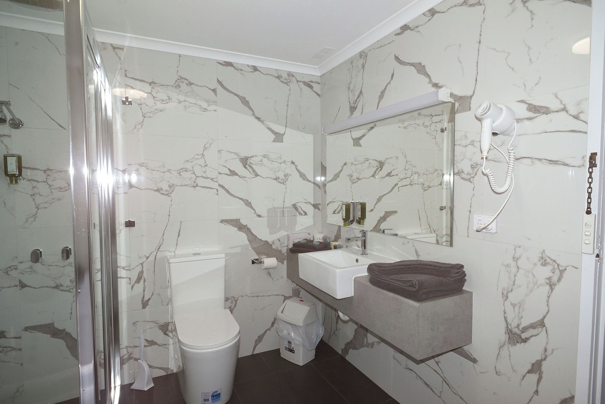 A bathroom with a marble backsplash, a white toilet, a sink, a mirror, and a hairdryer on the wall.