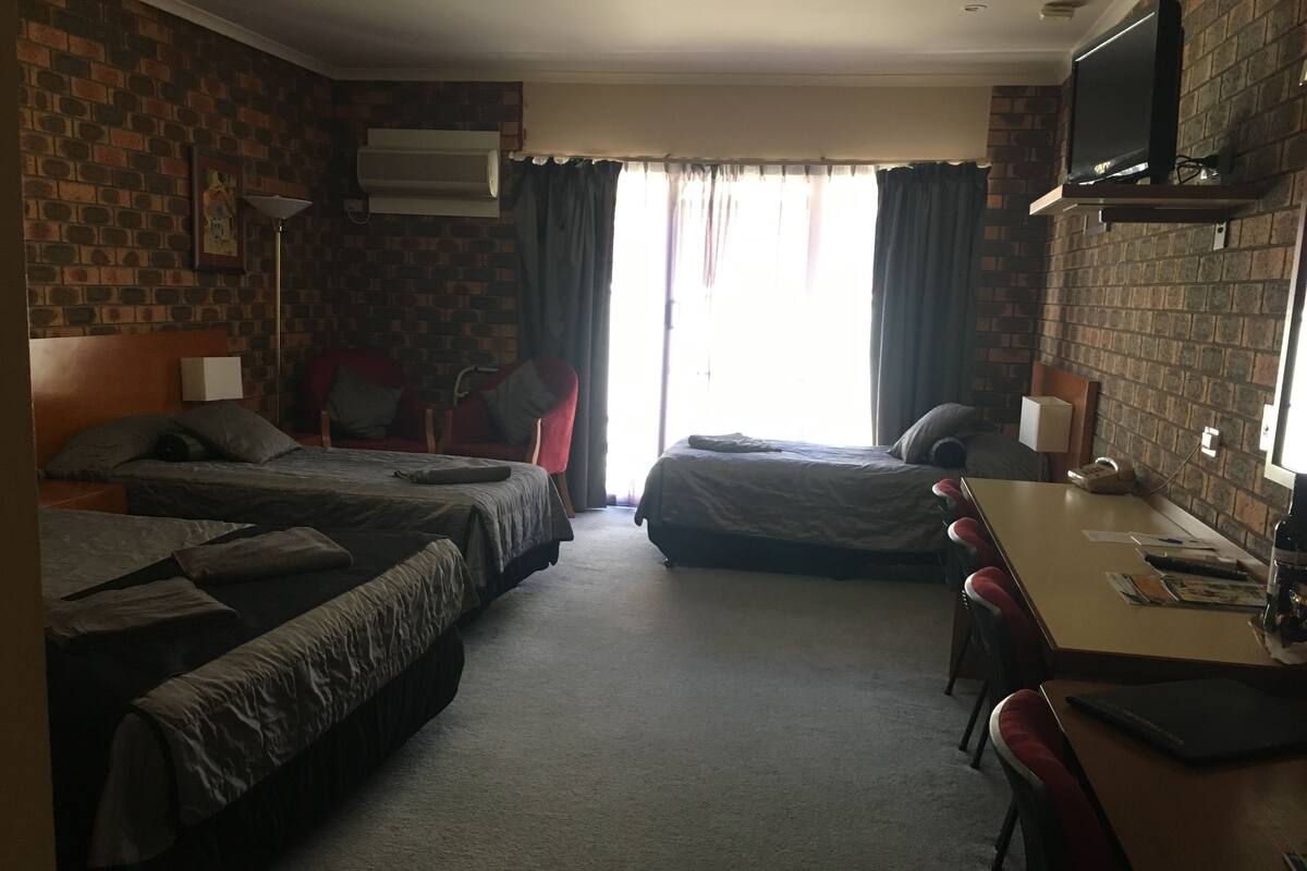 Hotellihuone, jossa on kaksi sänkyä, työpöytä, tuoli, televisio ja ikkuna, jossa on verhot.