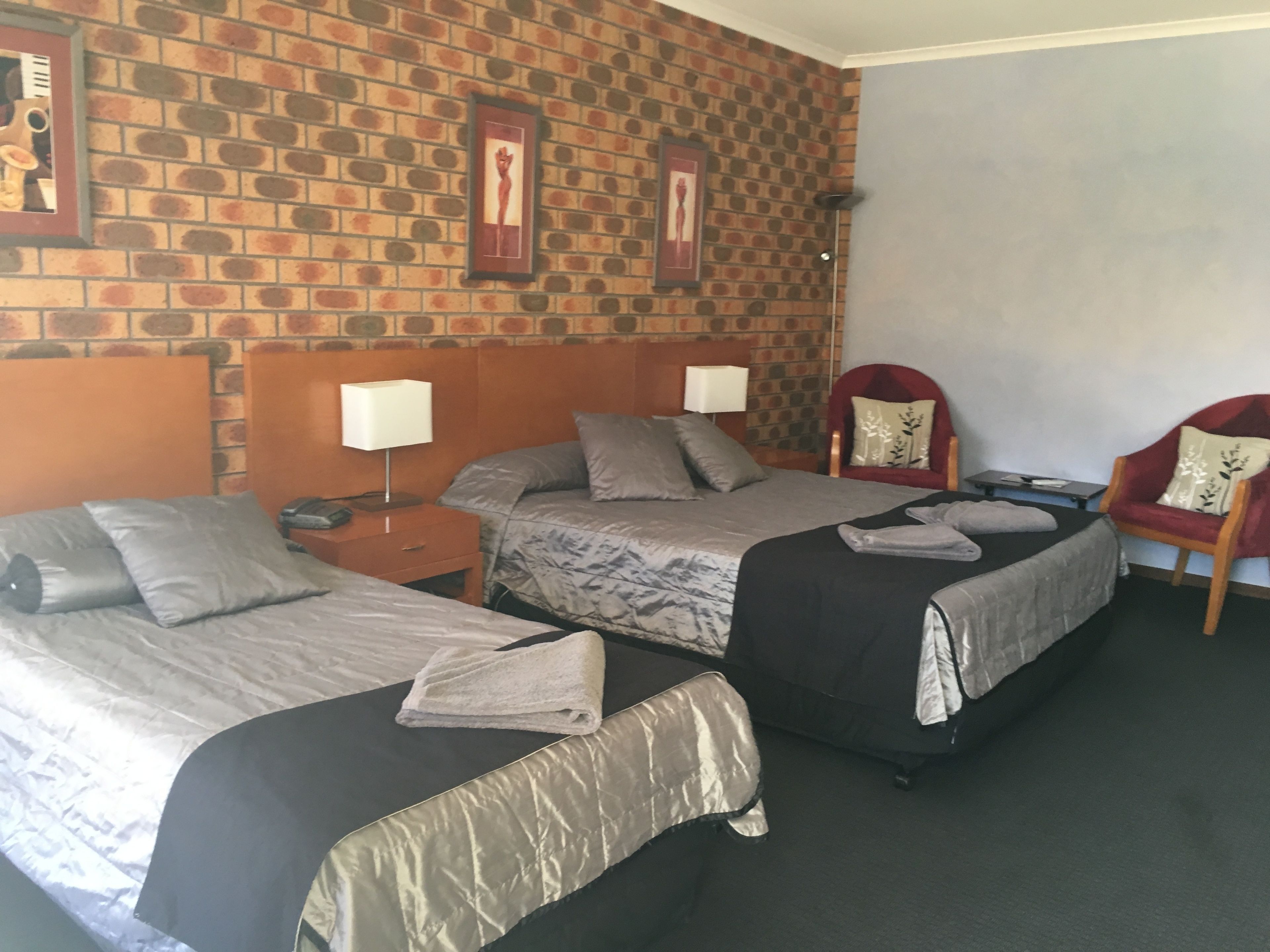 Habitación de hotel con dos camas, una pared de ladrillo y dos sillas.