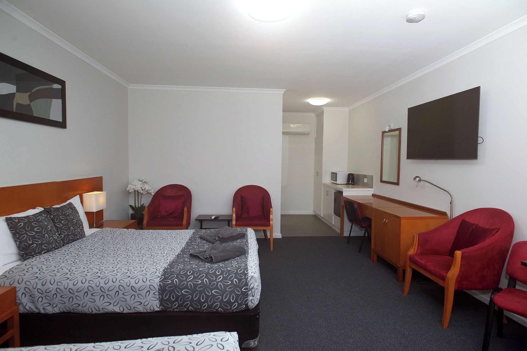 A hotel room with a bed, two red chairs, a desk with a computer, a TV, and a mirror.