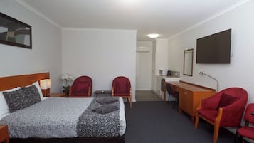 Una camera d'albergo con un letto, due poltrone rosse, una scrivania con un computer, una TV e uno specchio.