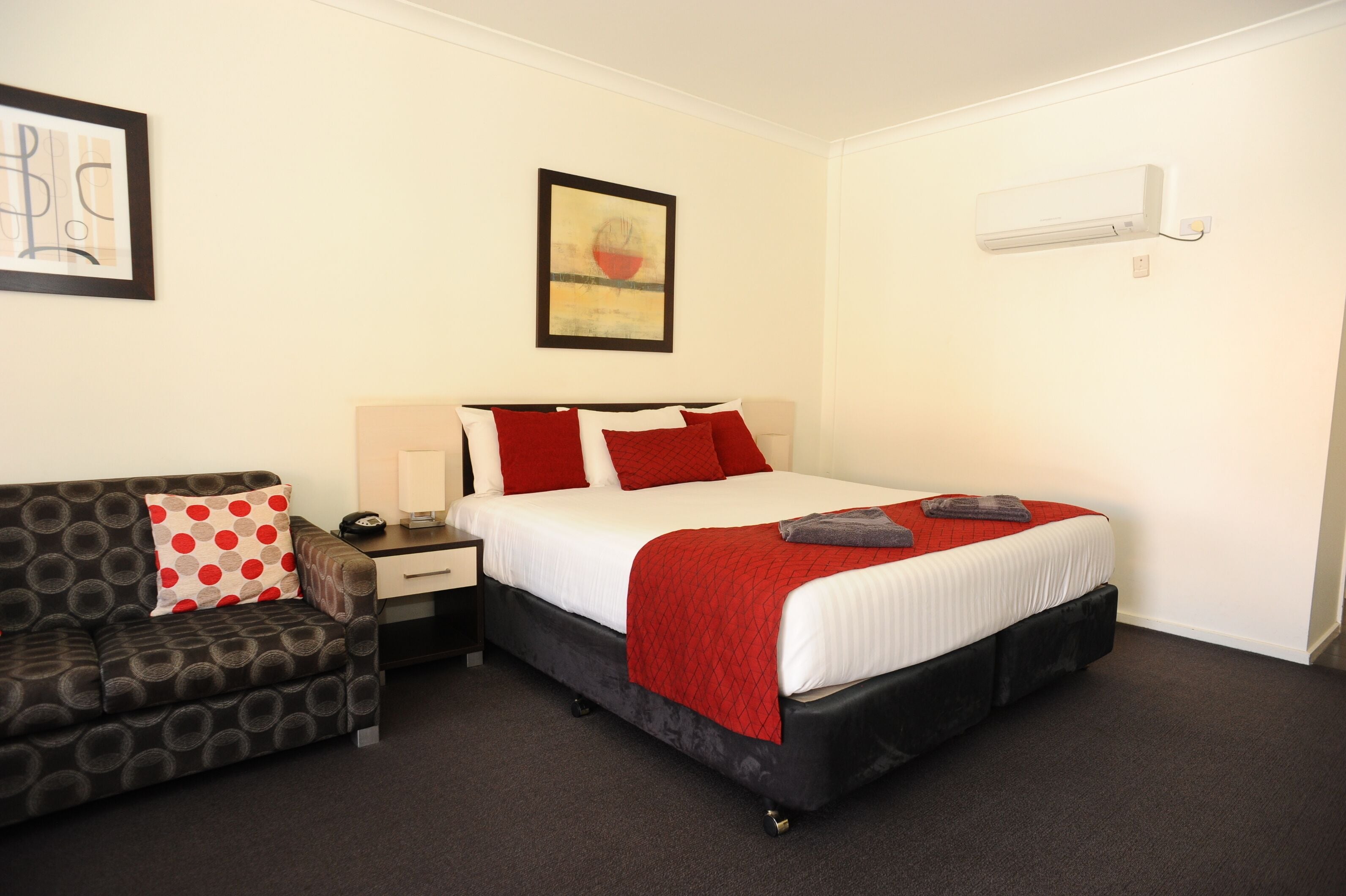 A hotel room with a bed, a nightstand, a desk, a chair, and a wall-mounted air conditioner.